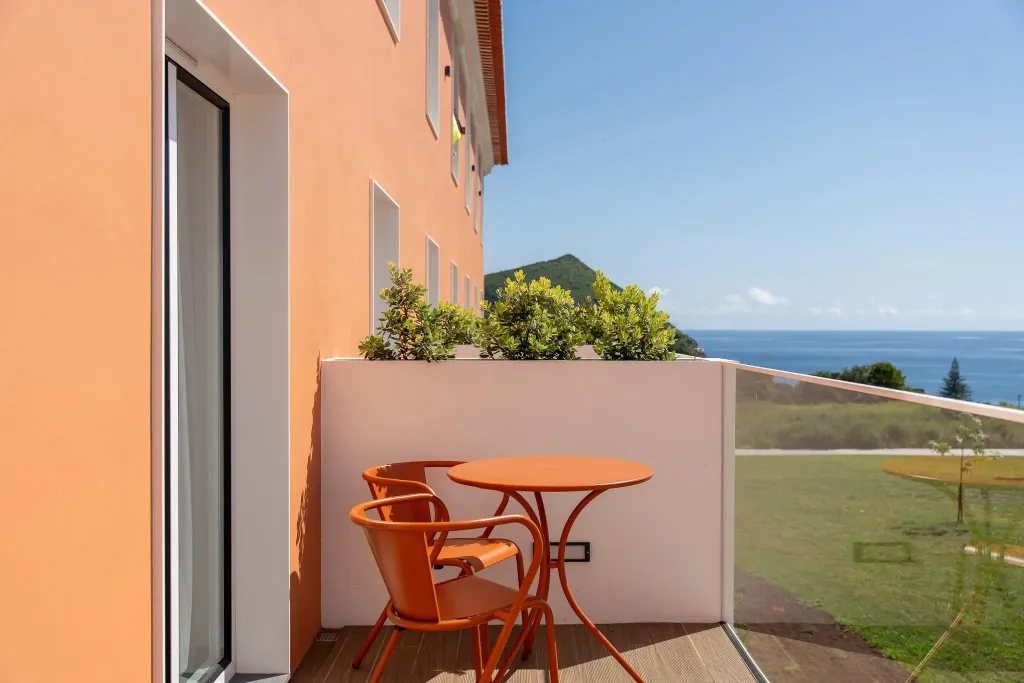 Une terrasse avec une table et des chaises offre une vue sur la mer et la végétation.