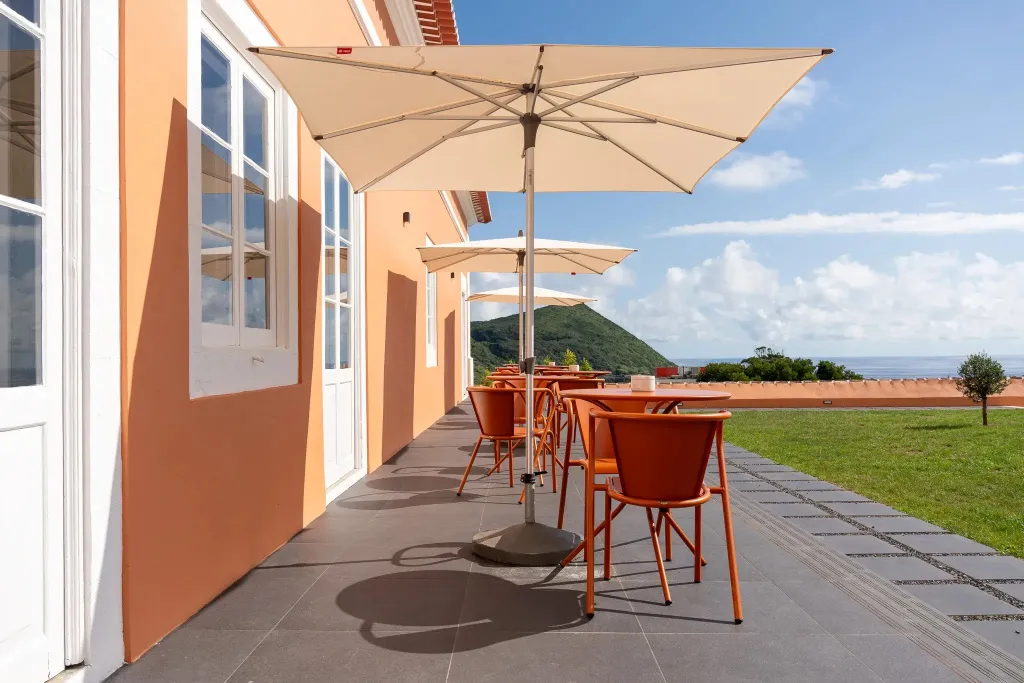 Terrasse ombragée avec tables et chaises donnant sur un paysage verdoyant.