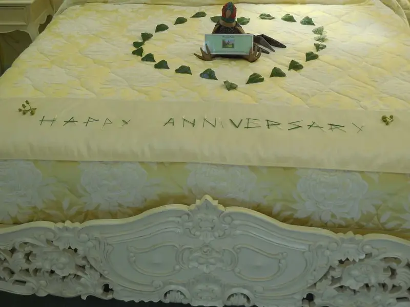 Un lit décoré pour un anniversaire de mariage avec des pétales et un cadeau.
