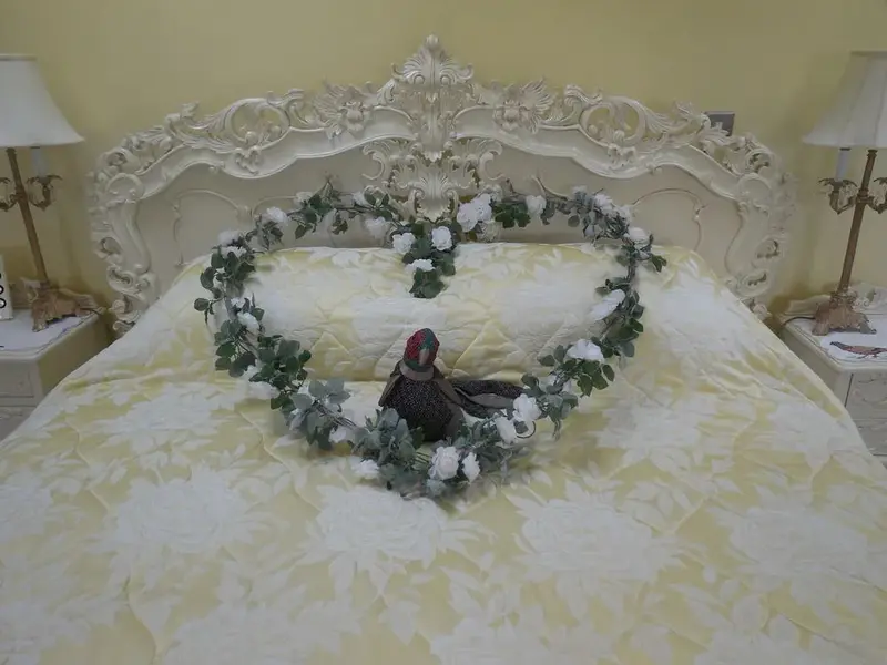 Un lit est decoré d'une guirlande florale en forme de cœur et d'une statuette d'oiseau.