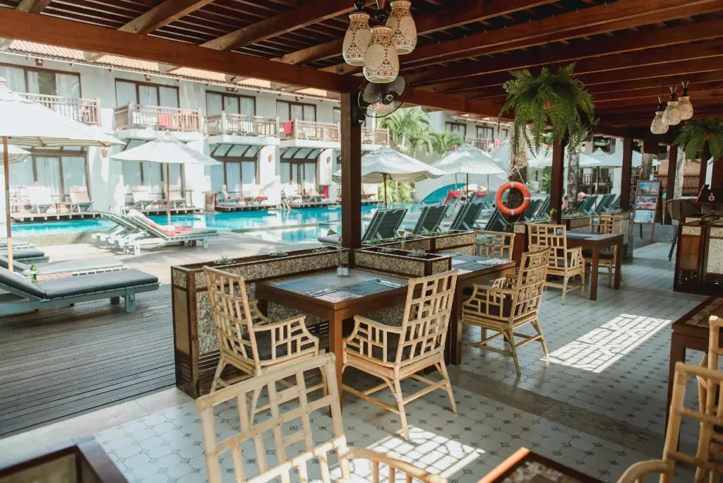 Terrasse ombragée avec tables et chaises en osier près d'une piscine.