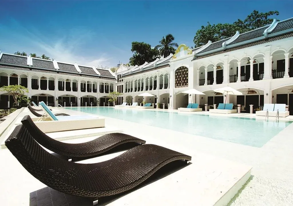 Transats noirs disposés au bord d'une piscine turquoise dans un complexe hôtelier blanc.