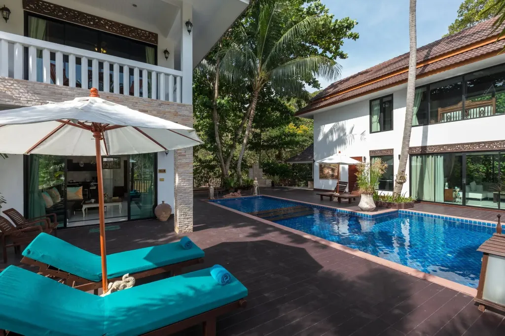 Transats bleus et parasols blancs bordent une piscine rectangulaire dans un jardin tropical.