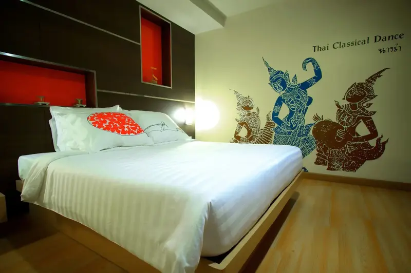Une chambre lumineuse avec un grand lit recouvert de draps blancs et des illustrations murales.