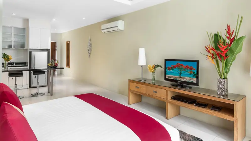 Une chambre lumineuse avec un lit rouge et blanc, une kitchenette et un meuble télévision.