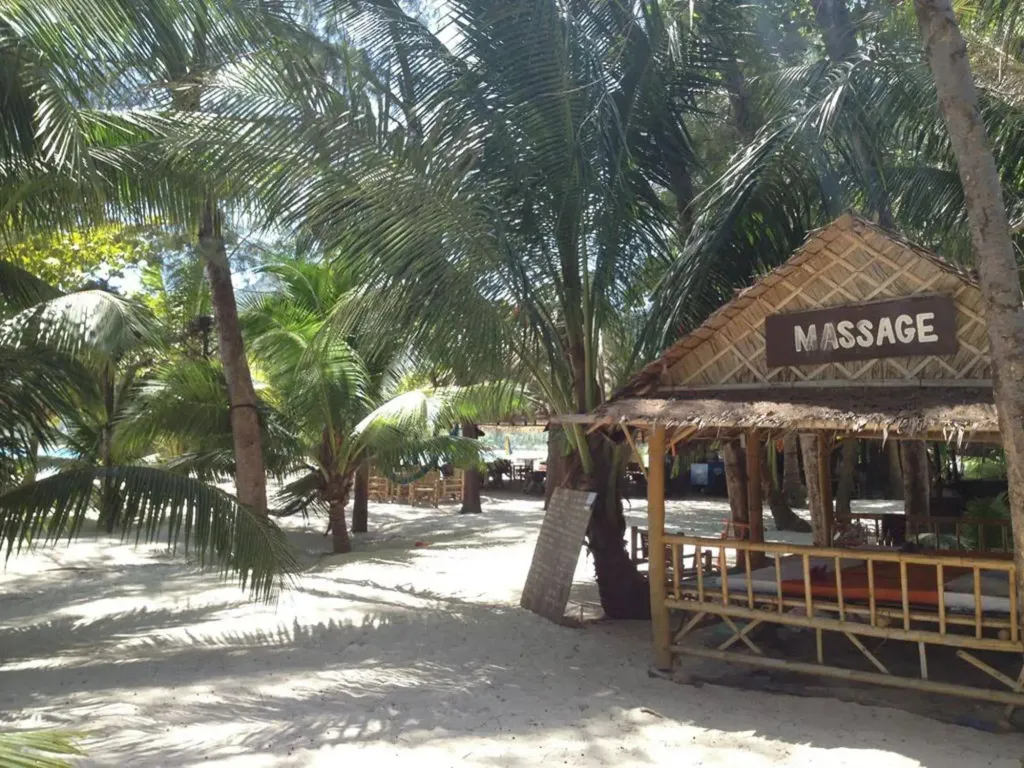 Cabane de massage sur une plage de sable blanc bordée de palmiers.
