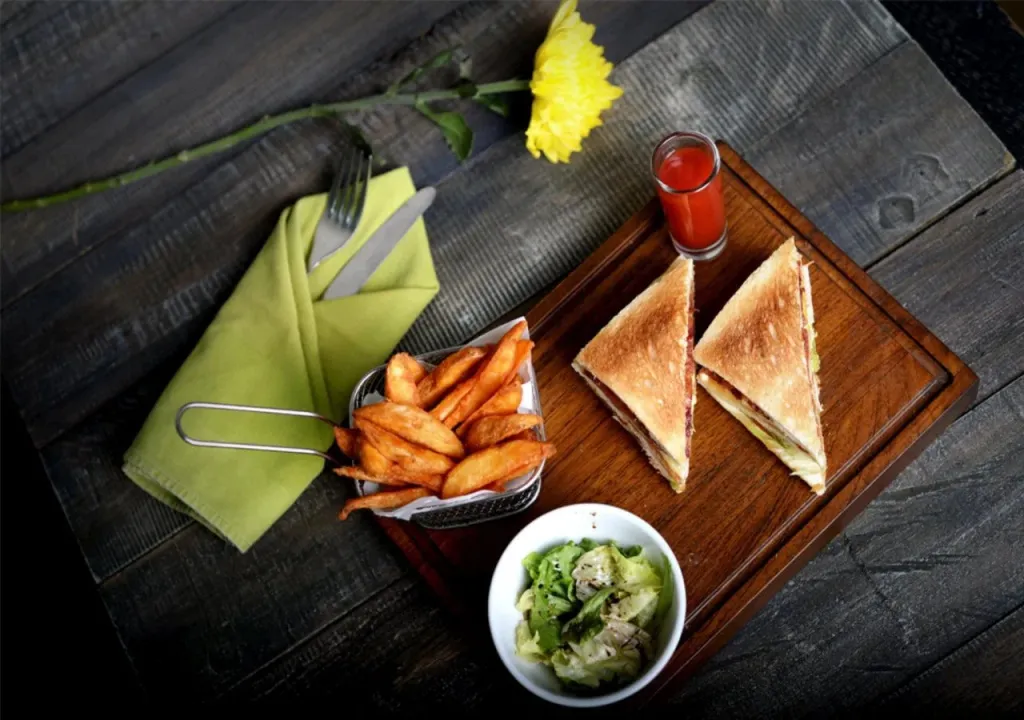 Assiette de sandwichs, frites et salade sur une planche en bois.
