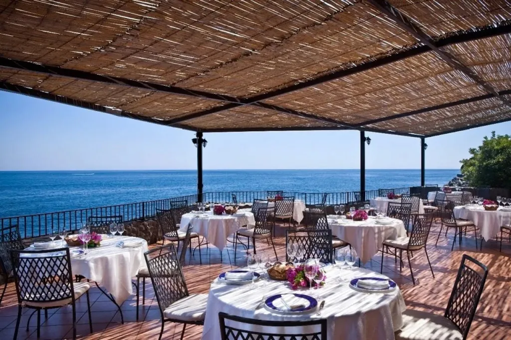 Une terrasse ombragée avec des tables dressées face à la mer.