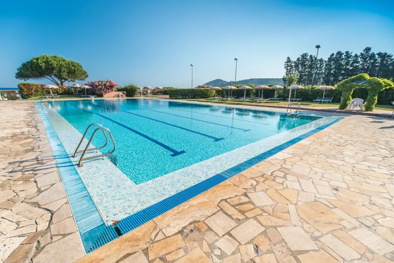 Une piscine rectangulaire entourée d'une terrasse carrelée et de transats.