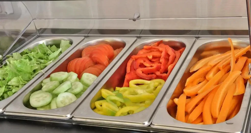 Des légumes frais coupés sont présentés dans des bacs en acier inoxydable.