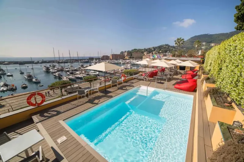 Terrasse avec piscine et vue sur un port de plaisance ensoleillé.