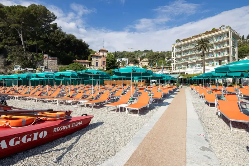 Transats orange alignés sur une plage de galets sous des parasols turquoise.