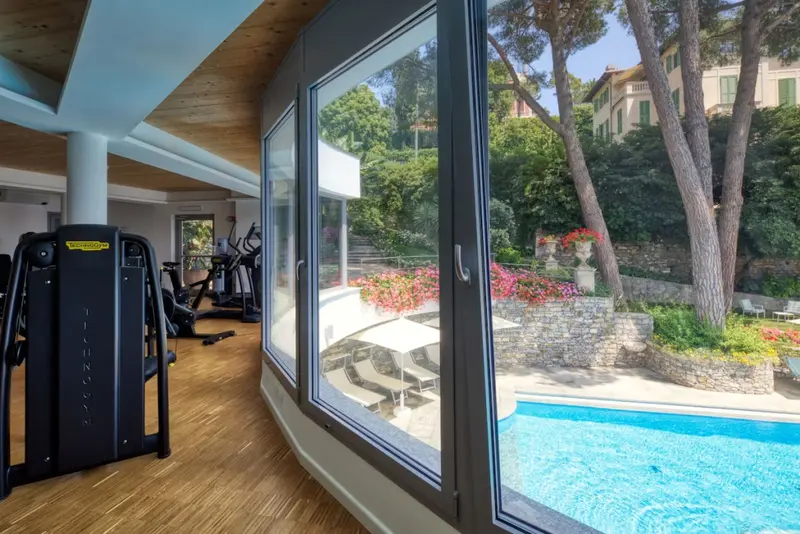 Une salle de sport lumineuse donne sur une piscine et un jardin fleuri.