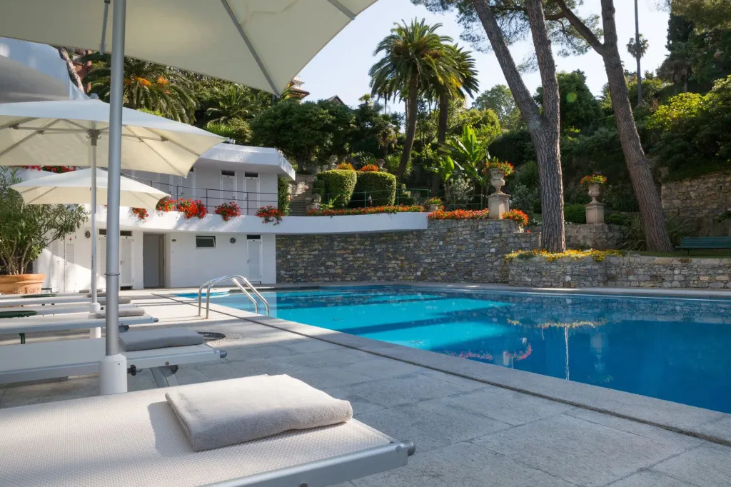Transats blancs disposés au bord d'une piscine bleue ombragée par des parasols.