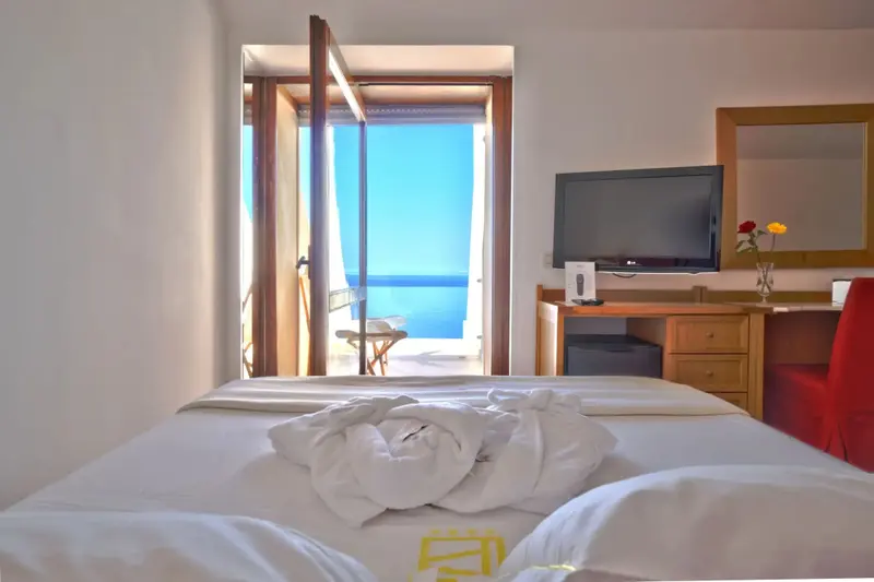 Une chambre lumineuse avec un lit fait et une vue sur la mer par une baie vitrée.