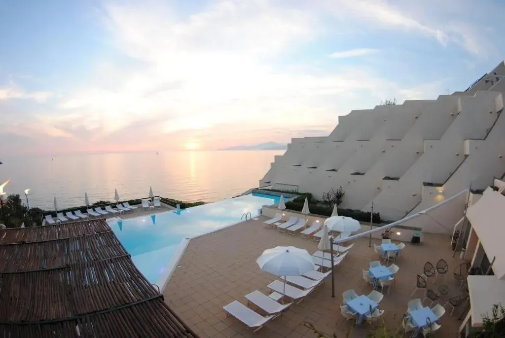 Vue aérienne d'une piscine à débordement surplombant la mer au coucher du soleil.