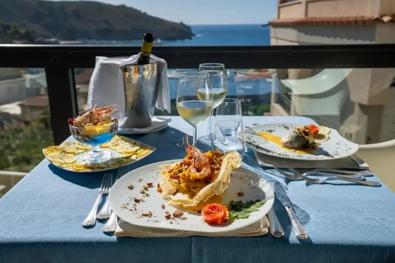 Une table dressée avec des plats de fruits de mer et du vin, vue sur la mer.