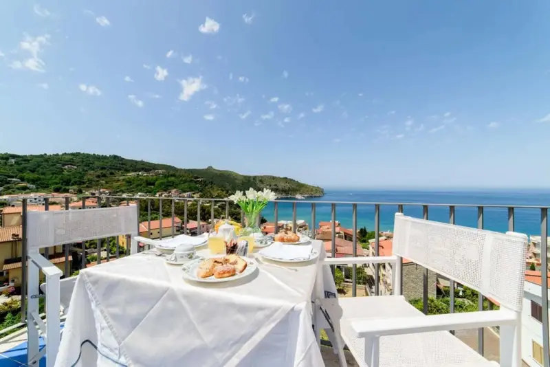 Une table est dressée pour le petit-déjeuner sur une terrasse ensoleillée avec vue sur la mer.