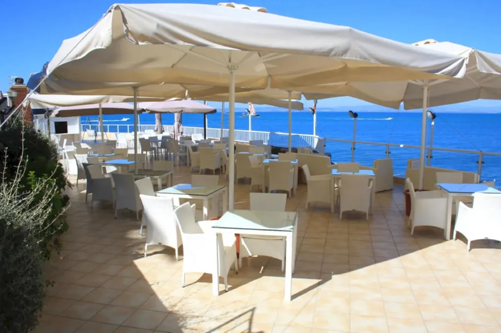 Terrasse ombragée avec tables et chaises donnant sur la mer.