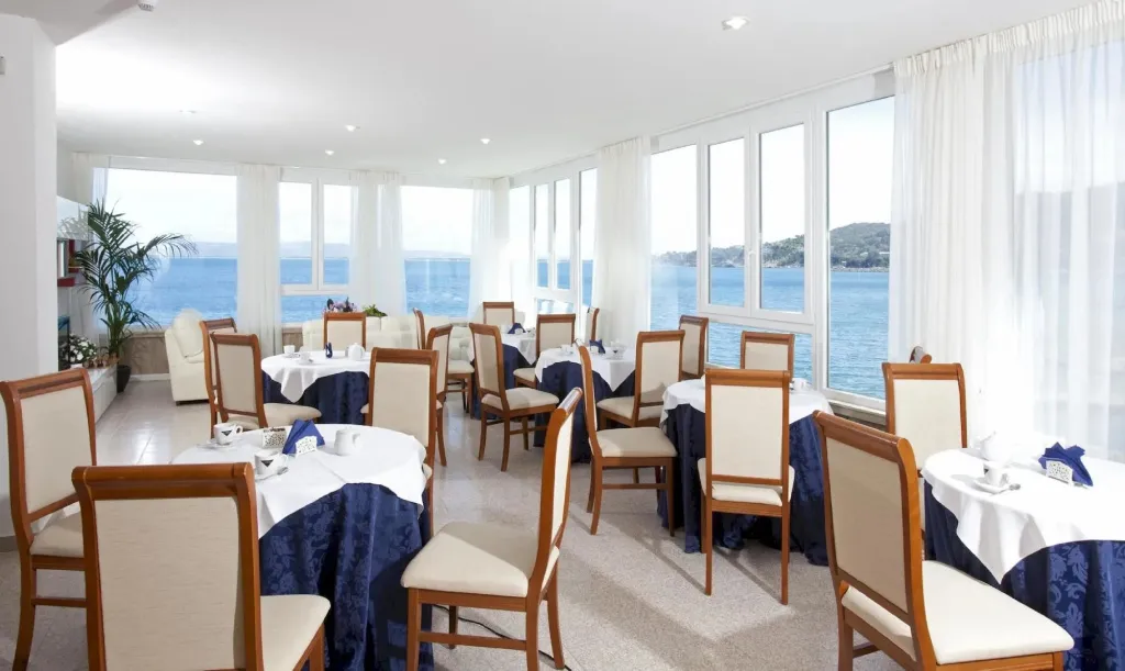 Une salle lumineuse avec des tables dressées devant de grandes baies vitrées donnant sur la mer.