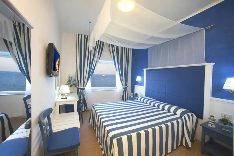 Une chambre lumineuse avec un lit recouvert d'un tissu rayé et une vue sur la mer.