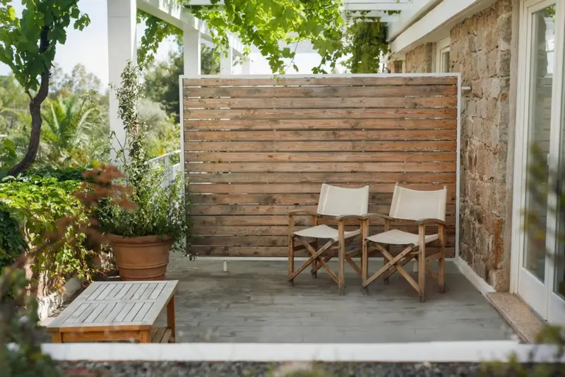 Deux chaises en bois et une petite table basse sur une terrasse ombragée.