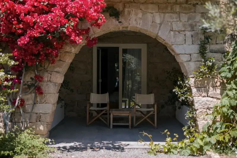 Une arche en pierre fleurie donne sur un espace de repos avec deux fauteuils et une petite table.