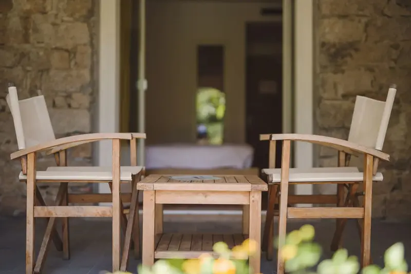 Deux fauteuils en bois et une petite table basse sur une terrasse ombragée.
