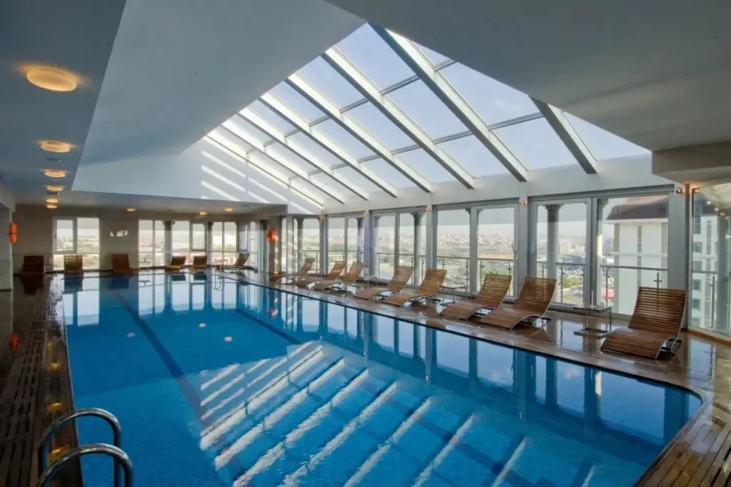 Une piscine intérieure lumineuse avec des transats alignés le long de la fenêtre.