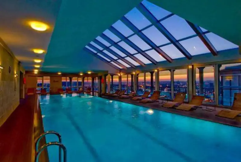 Une piscine intérieure lumineuse offre une vue sur la ville au coucher du soleil.
