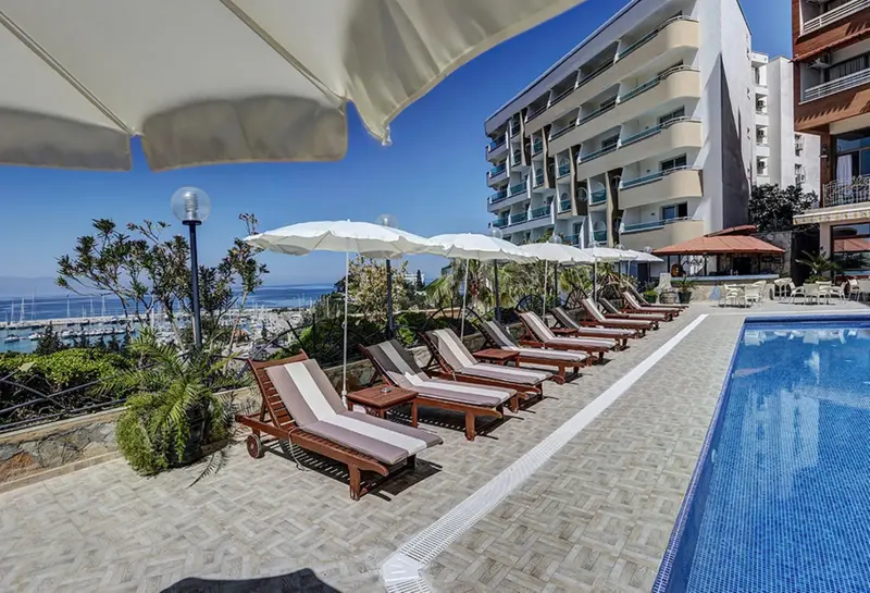 Transats alignés au bord d'une piscine avec vue sur la mer et un bâtiment en arrière-plan.
