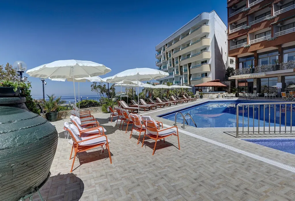 Transats oranges disposés autour d'une piscine ensoleillée avec vue sur la mer.