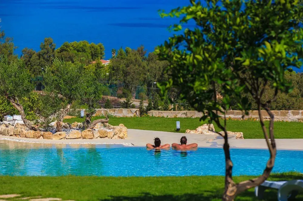 Deux personnes se détendent dans une piscine bordée de verdure.