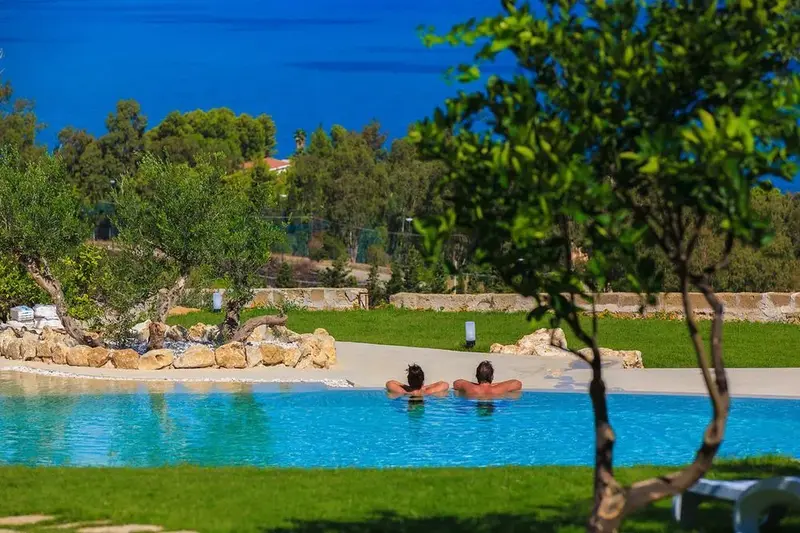 Deux personnes se détendent dans une piscine bordée de verdure.