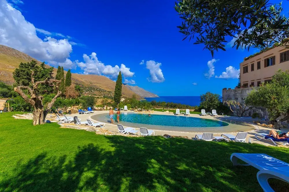 Une piscine bordée de transats dans un jardin verdoyant avec vue sur la mer.