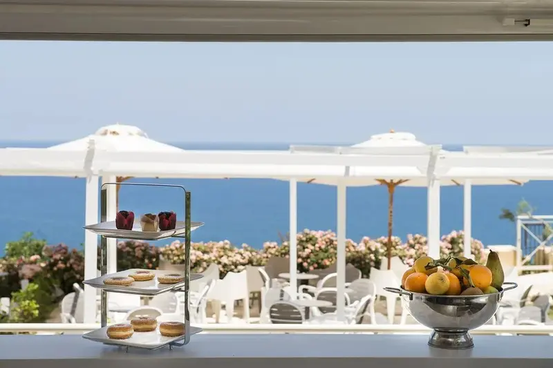 Une table garnie de pâtisseries et de fruits en vue sur la mer.