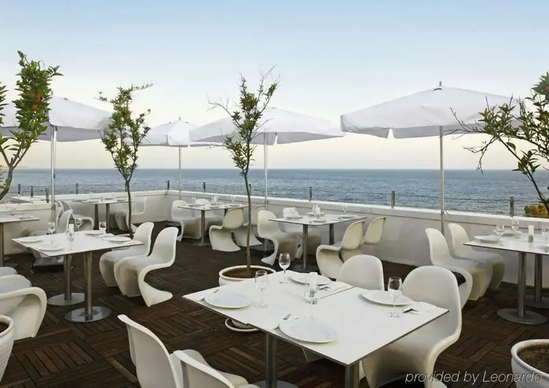 Terrasse lumineuse avec tables et chaises blanches face à la mer.
