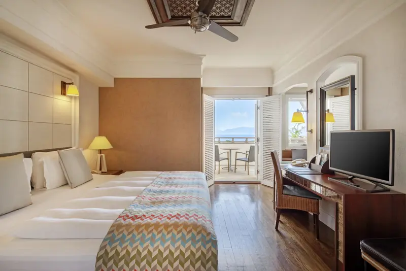 Une chambre lumineuse avec un grand lit et un balcon donnant sur la mer.