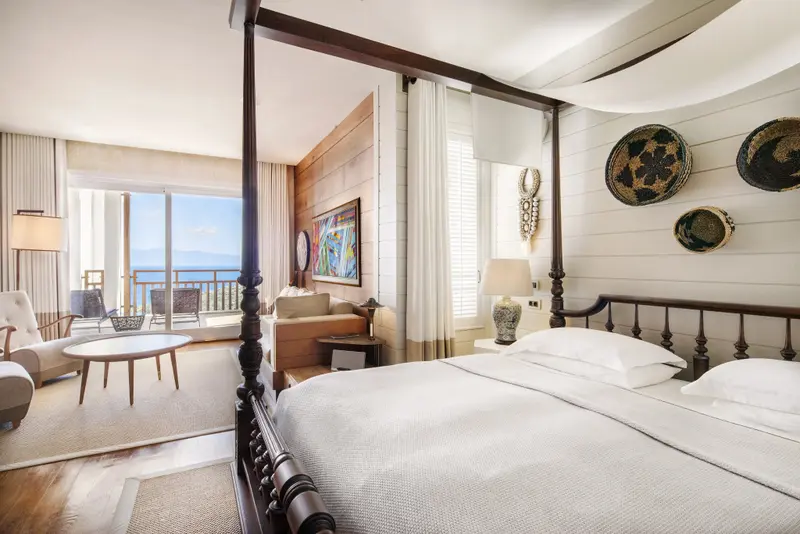 Une chambre lumineuse avec un grand lit à baldaquin donnant sur une vue mer.