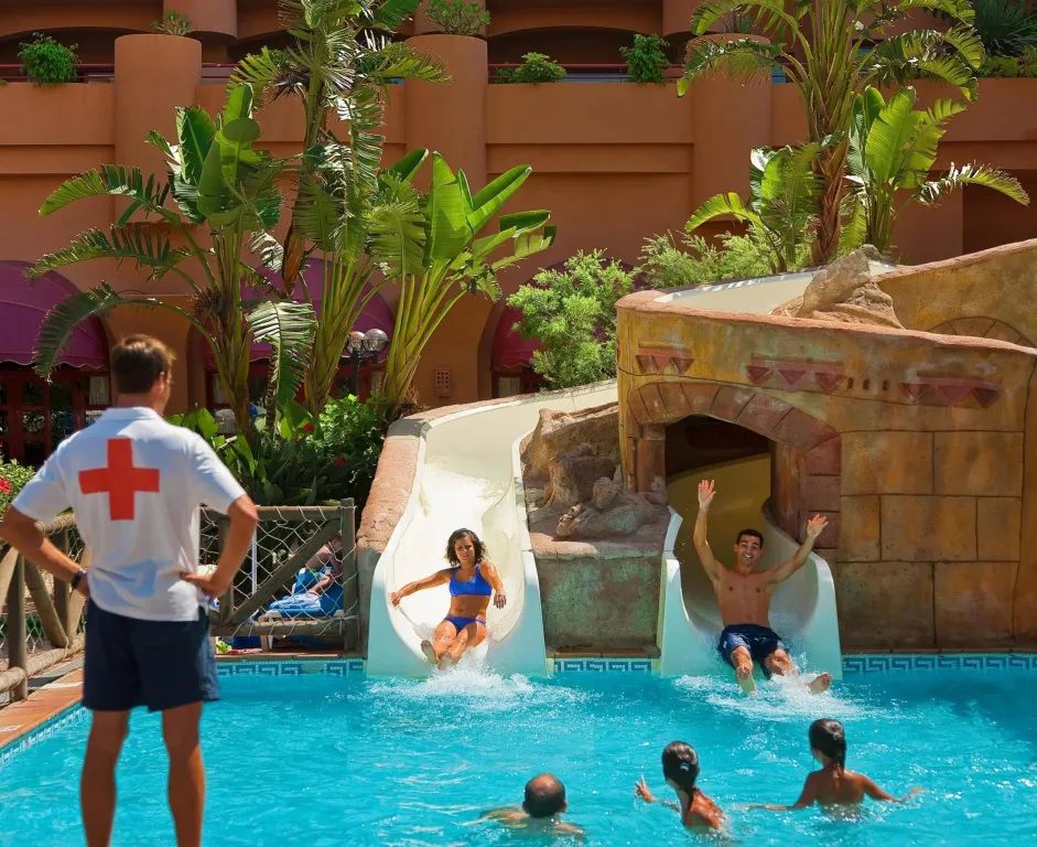 Une piscine avec deux toboggans et des personnes s'amusant dans l'eau.