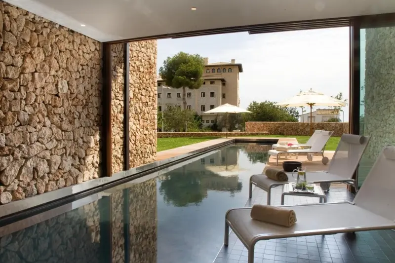 Piscine intérieure avec vue sur un jardin et un bâtiment.