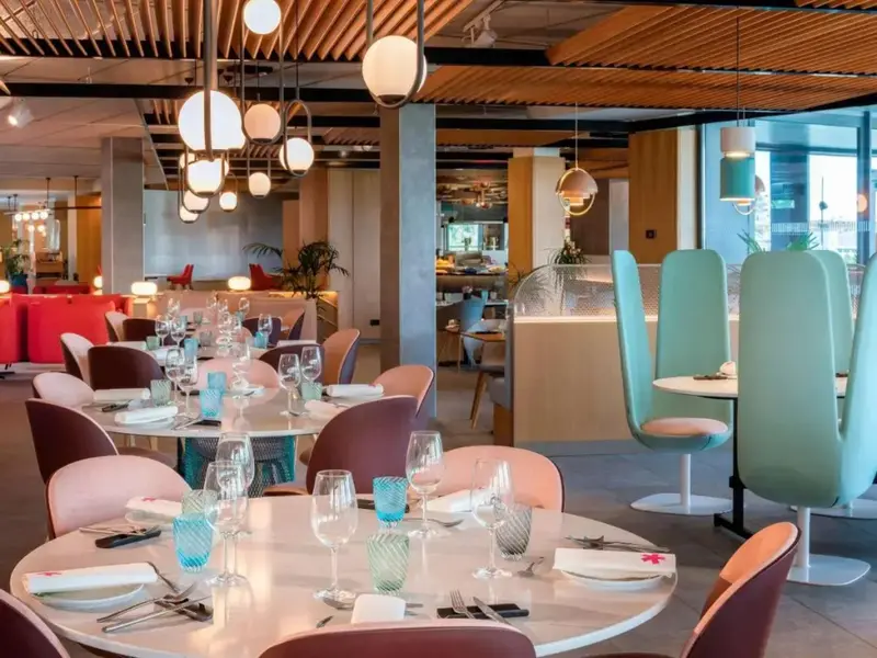 Une salle lumineuse est aménagée avec des tables rondes et des chaises colorées.