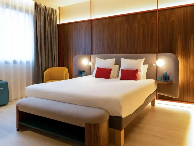 Une chambre lumineuse avec un grand lit recouvert d'une couette blanche et de coussins rouges.