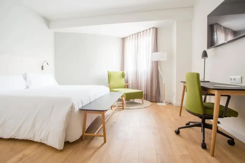 Une chambre lumineuse avec un lit, un bureau et un fauteuil.