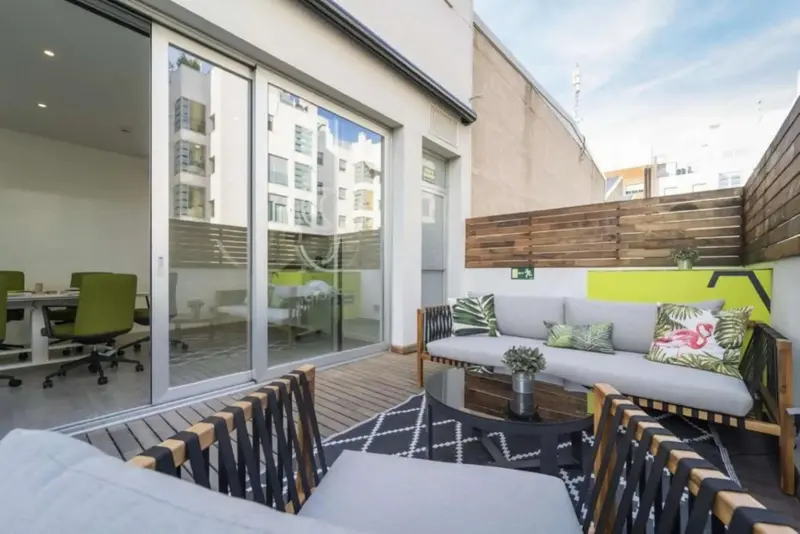 Espace extérieur aménagé avec salon et table basse, donnant sur un bureau vitré.