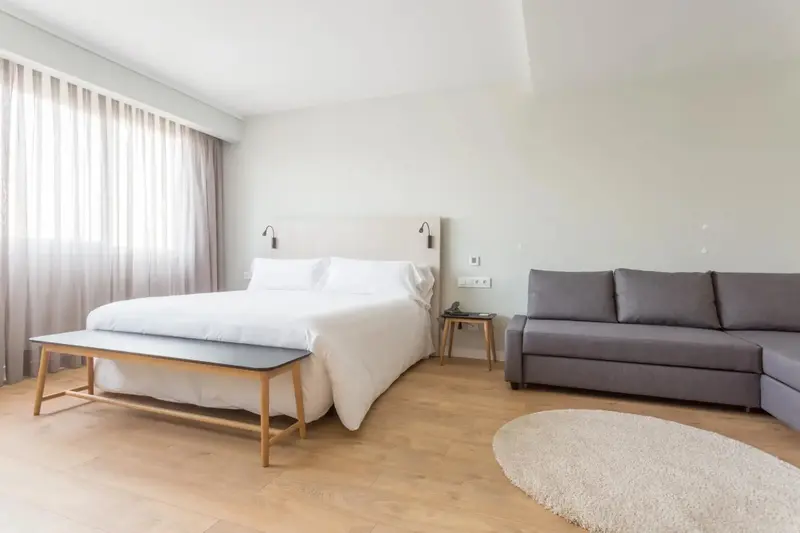 Une chambre lumineuse avec un grand lit et un canapé d'angle.