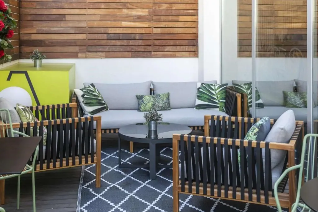 Espace de détente extérieur avec mobilier en bois et coussins à motifs.