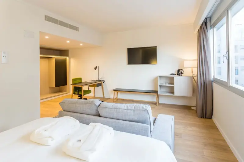 Espace de vie lumineux avec canapé, bureau et télévision.