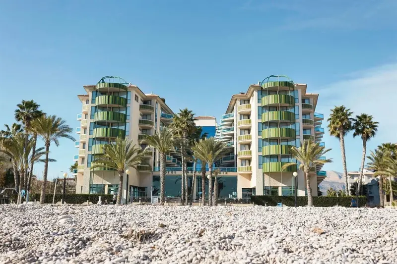 Bâtiment moderne avec des balcons verdoyants face à une plage de galets.