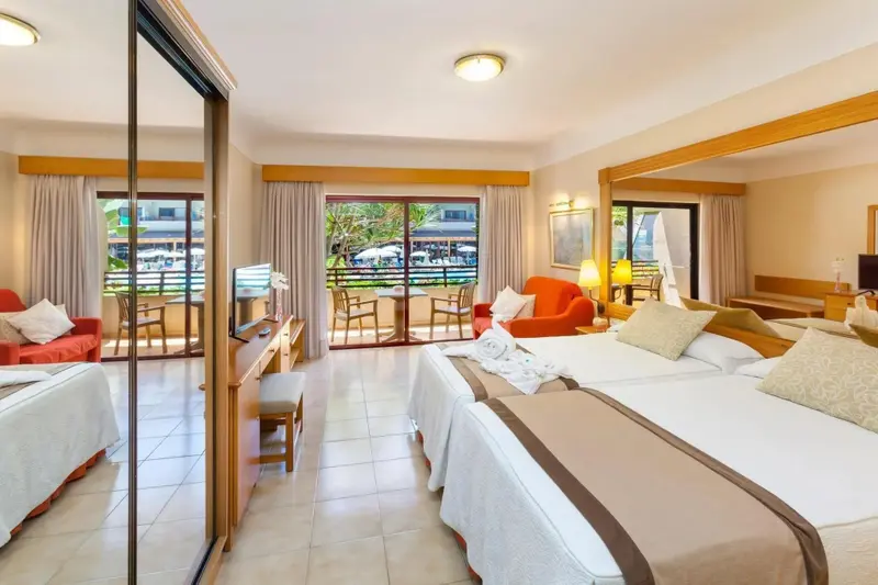 Une chambre lumineuse avec un lit double et un coin salon donnant sur une terrasse.